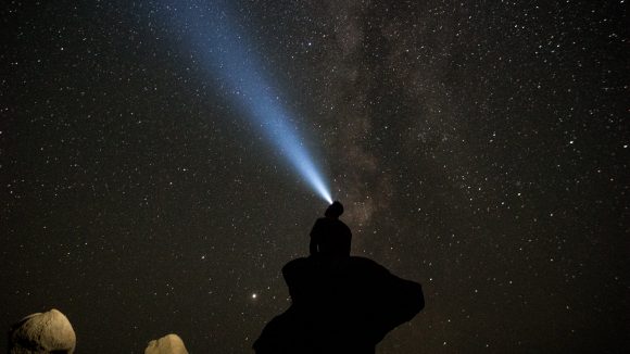 silhouette of man sitting on rock under starry night